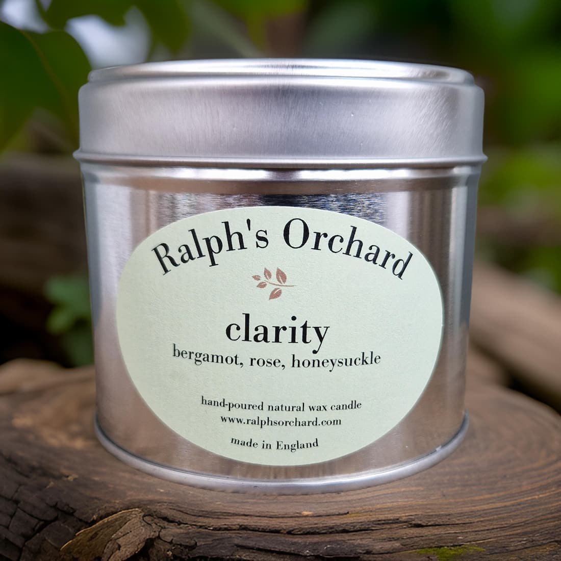 Candle tin labeled 'Ralph's Orchard Clarity' on a wooden surface with a natural background