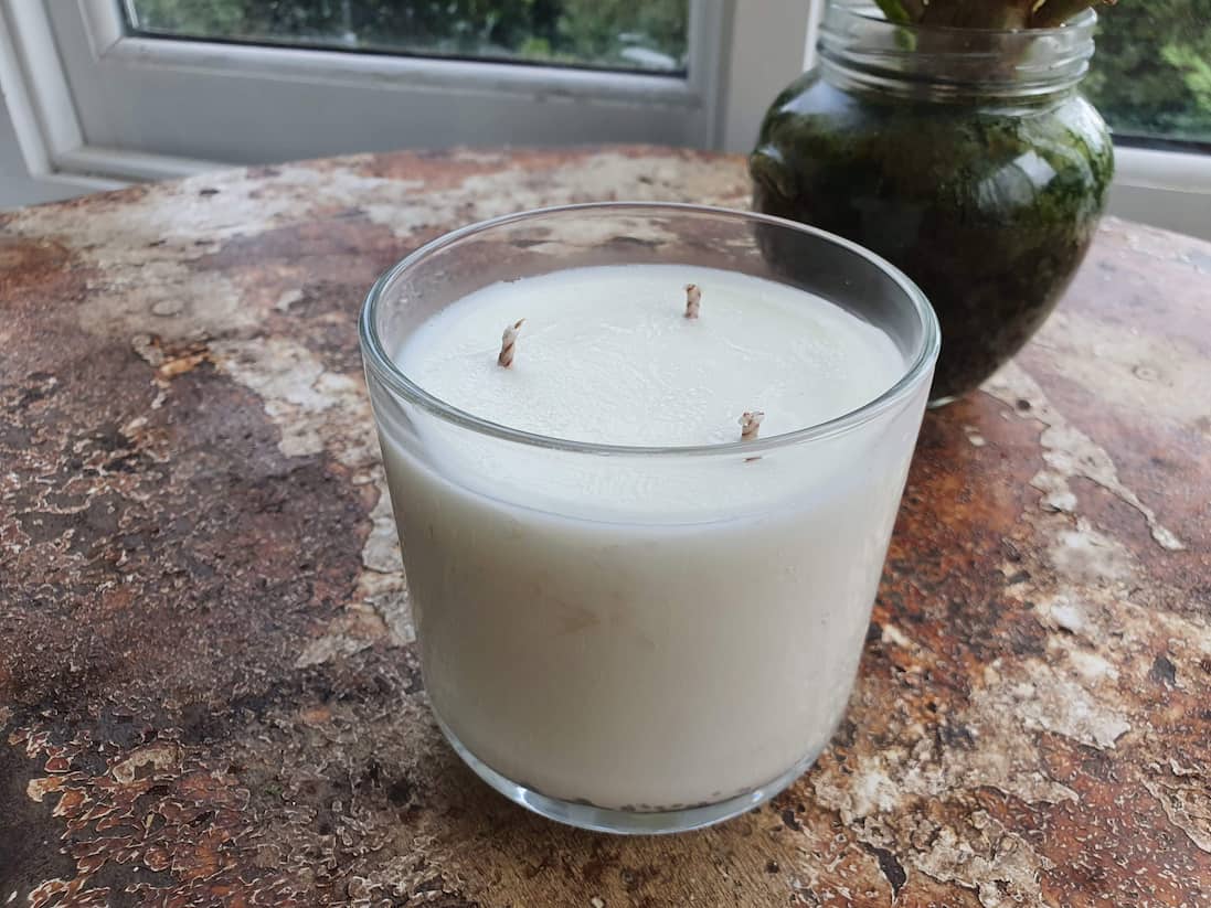 White candle in a glass jar on a textured surface with a blurred background