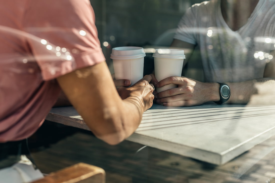 Two people holding hands across a table with coffee cups.
