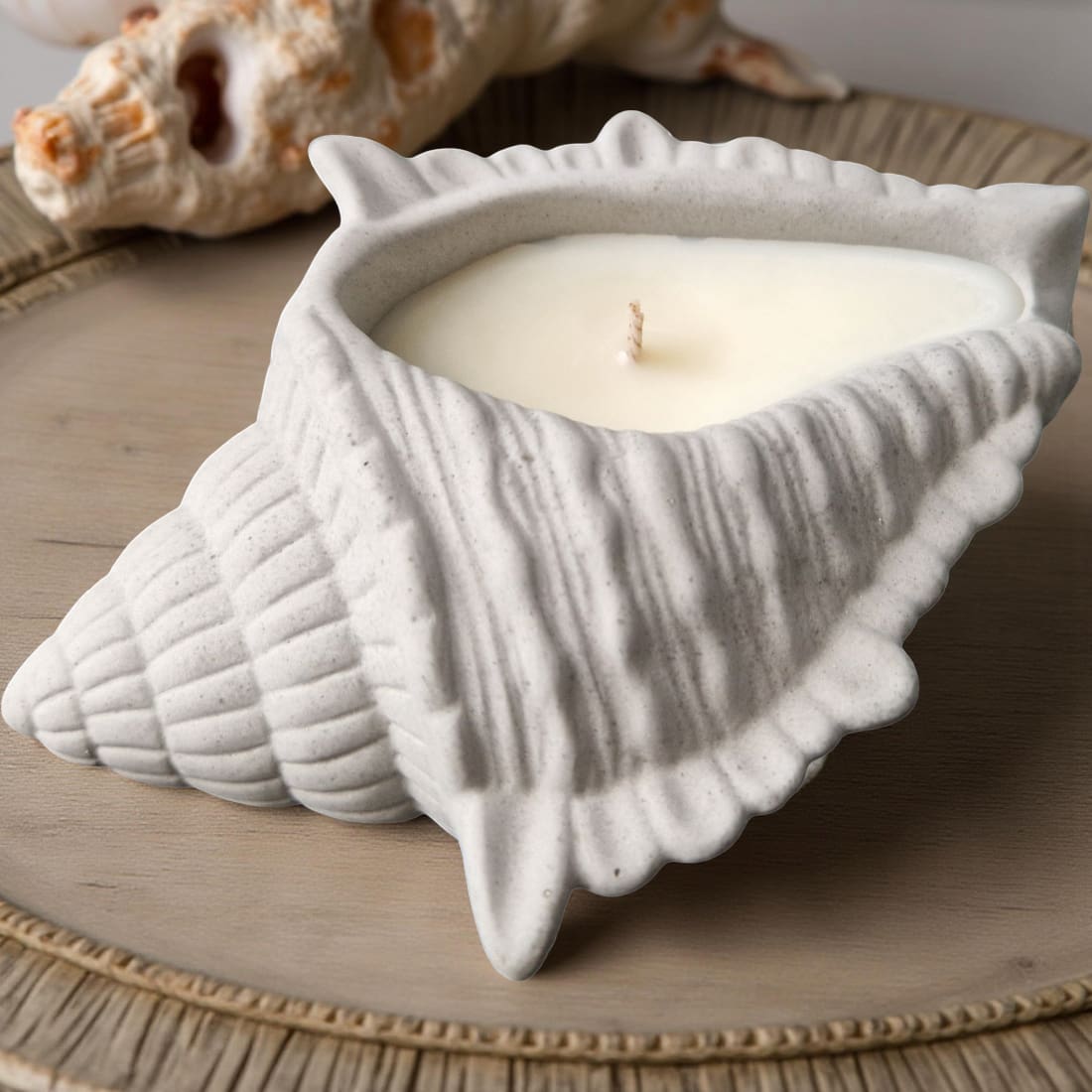 Ceramic shell-shaped candle holder with a candle inside on a wooden surface.