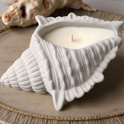 Ceramic shell-shaped candle holder with a candle inside on a wooden surface.