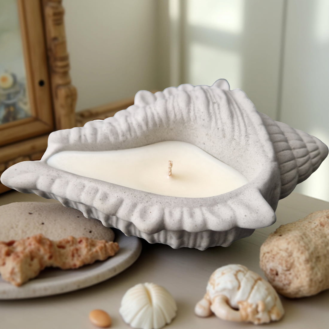 Shell-shaped candle on a surface with decorative shells and a framed picture in the background