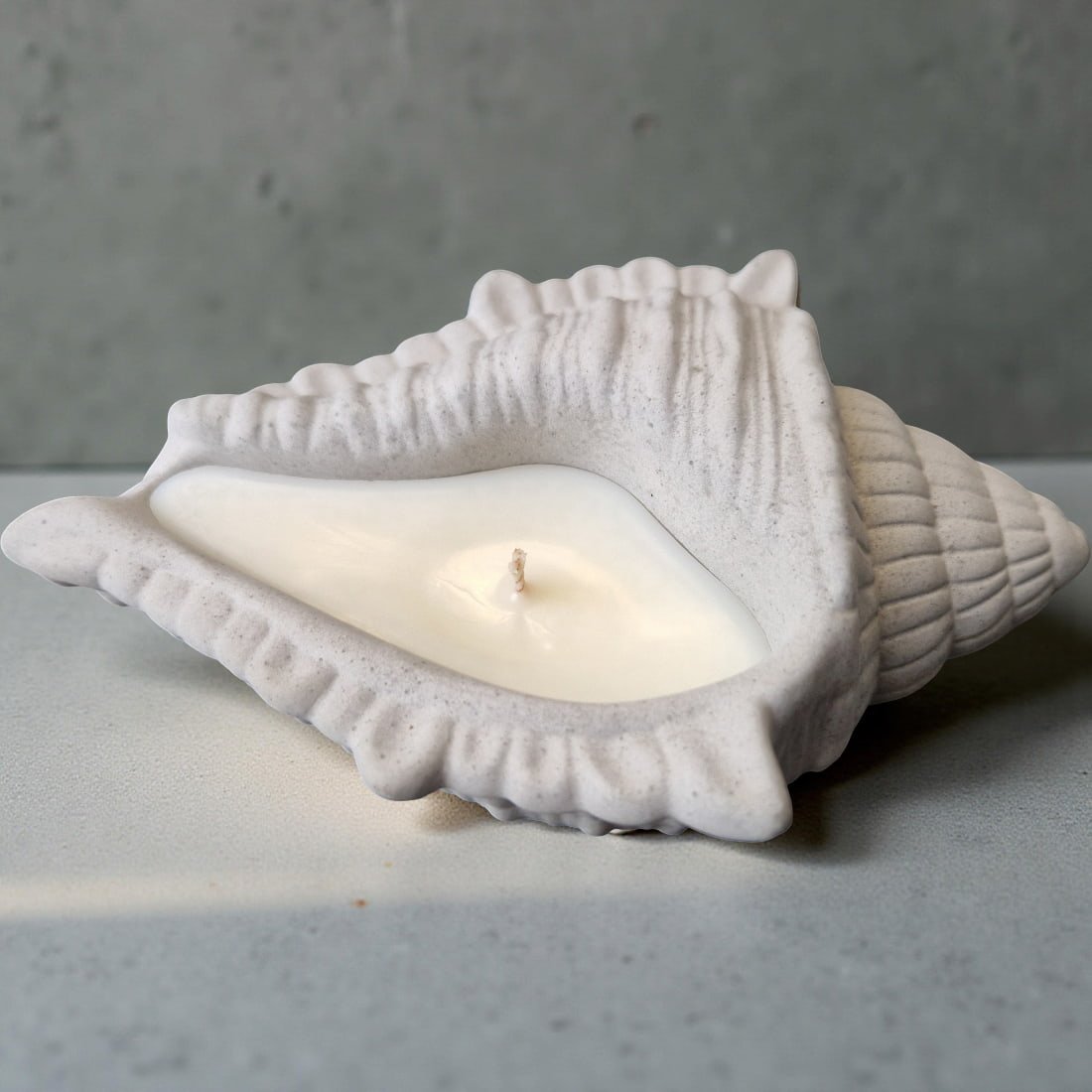 White ceramic shell with a candle inside on a gray surface