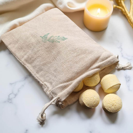 Beige drawstring bag with bath bombs on a marble surface next to a lit candle.