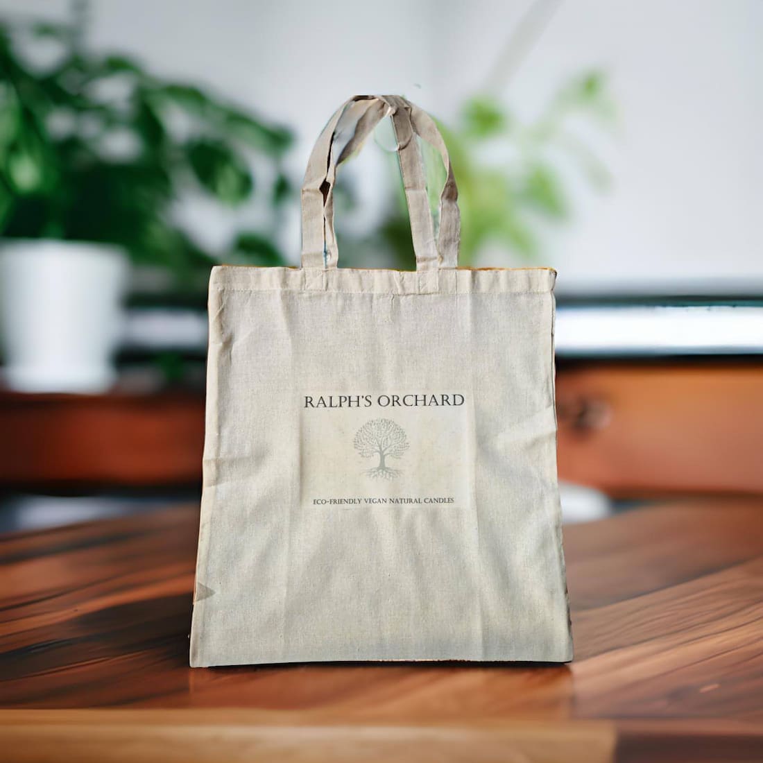 Beige tote bag with 'Ralph's Orchard' branding on a wooden surface with a blurred background