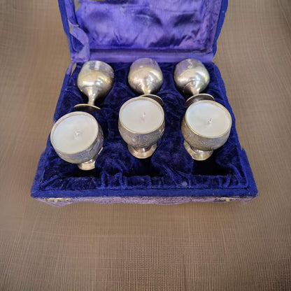 Set of six silver candle holders with white candles in a blue velvet box on a wooden surface.