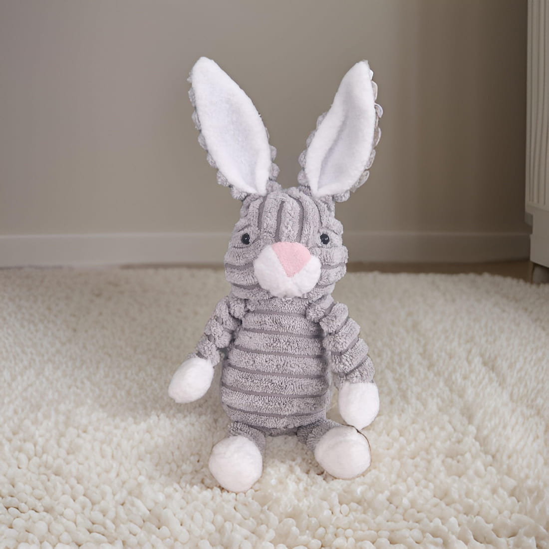 Gray plush bunny toy with white ears and paws on a beige carpet