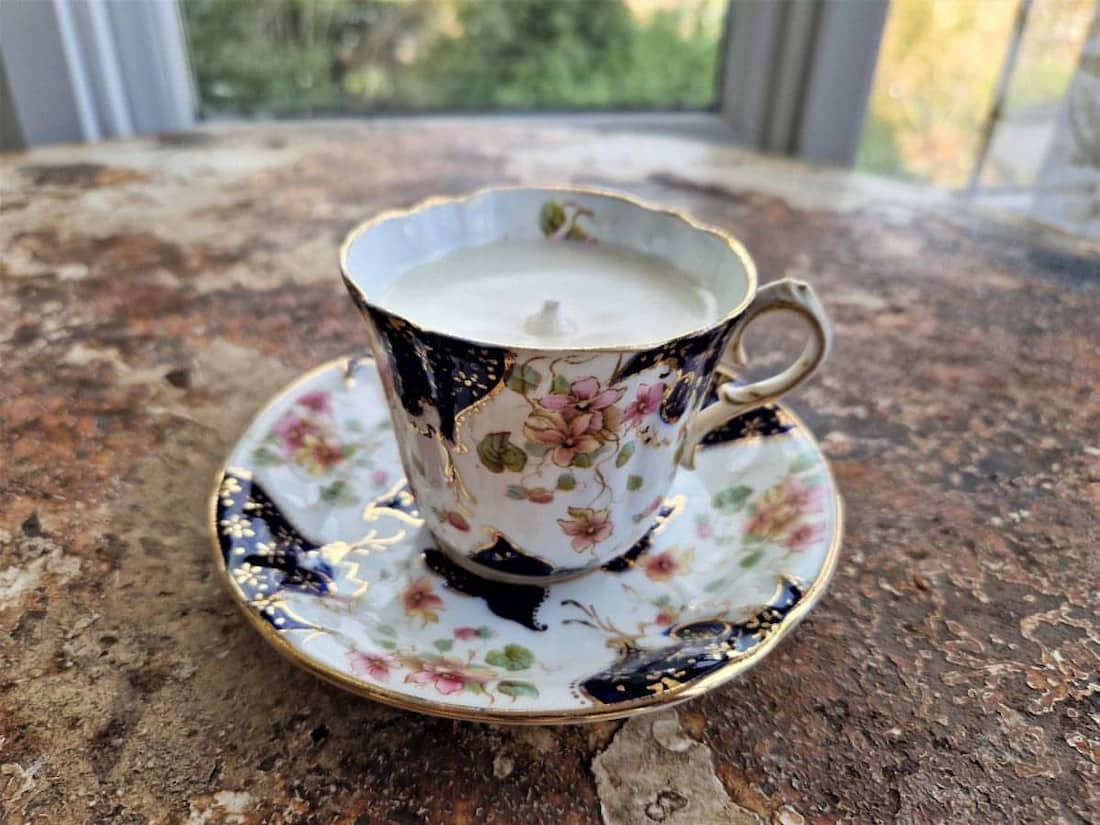 Decorative teacup and saucer with a candle inside on a stone surface.