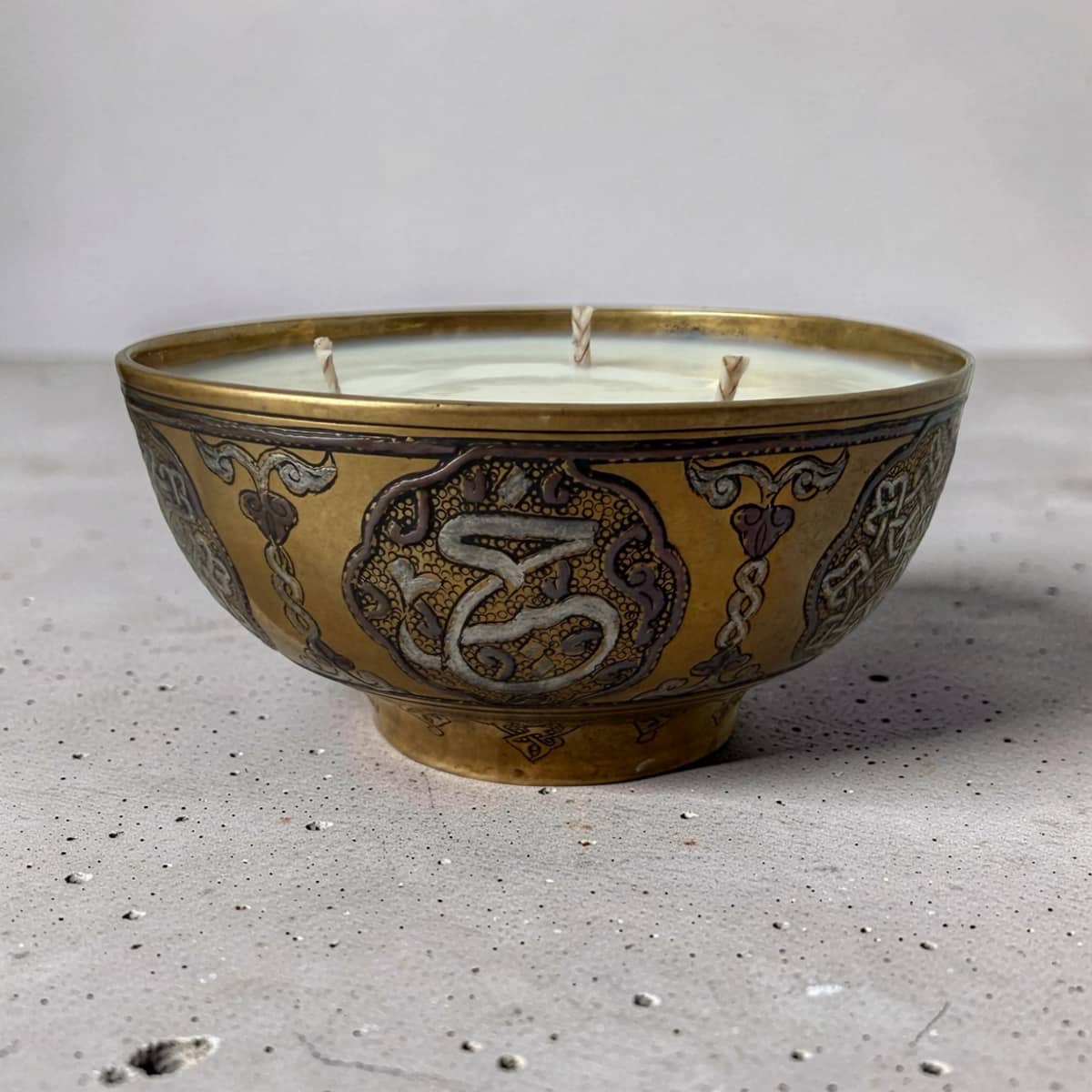 Decorative candle in a gold and black bowl on a textured surface