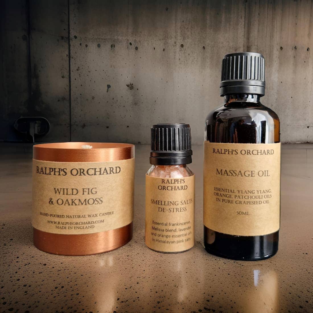 Three Ralph's Orchard products including a candle, deodorant stick, and massage oil on a textured surface.