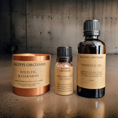 Three Ralph's Orchard products including a candle, deodorant stick, and massage oil on a textured surface.