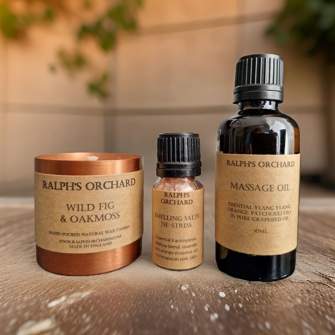 Three Ralph's Orchard products including a candle, salves, and massage oil on a wooden surface.