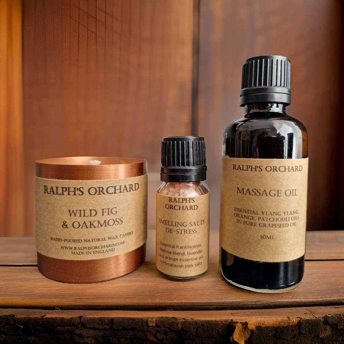 Three Ralph's Orchard products including a candle, salves, and massage oil on a wooden surface.