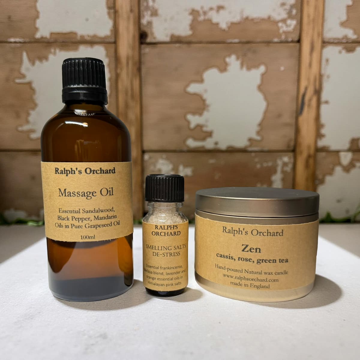 Three Ralph's Orchard products including massage oil, calming salts, and a candle on a textured surface.