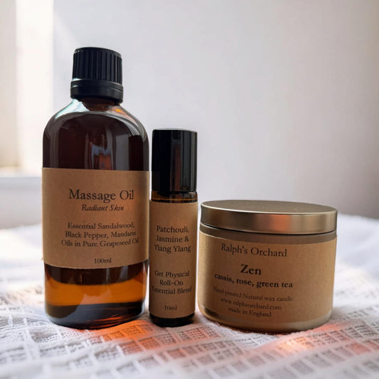 Three wellness products including a massage oil bottle, roller bottle, and candle on a textured surface.