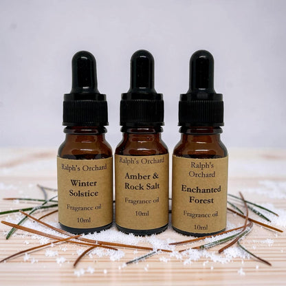 Three bottles of Ralph's Orchard fragrance oils on a wooden surface with decorative elements.