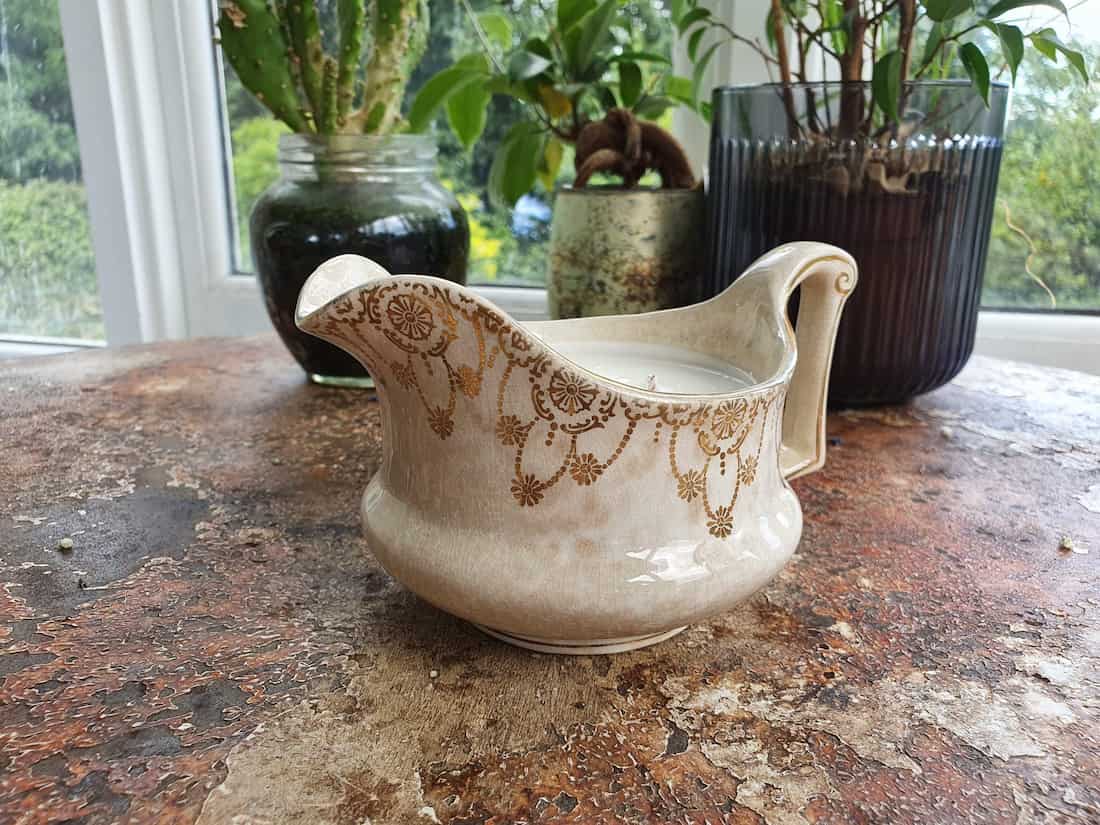 Vintage cream pitcher with gold patterns on a rustic surface with plants in the background