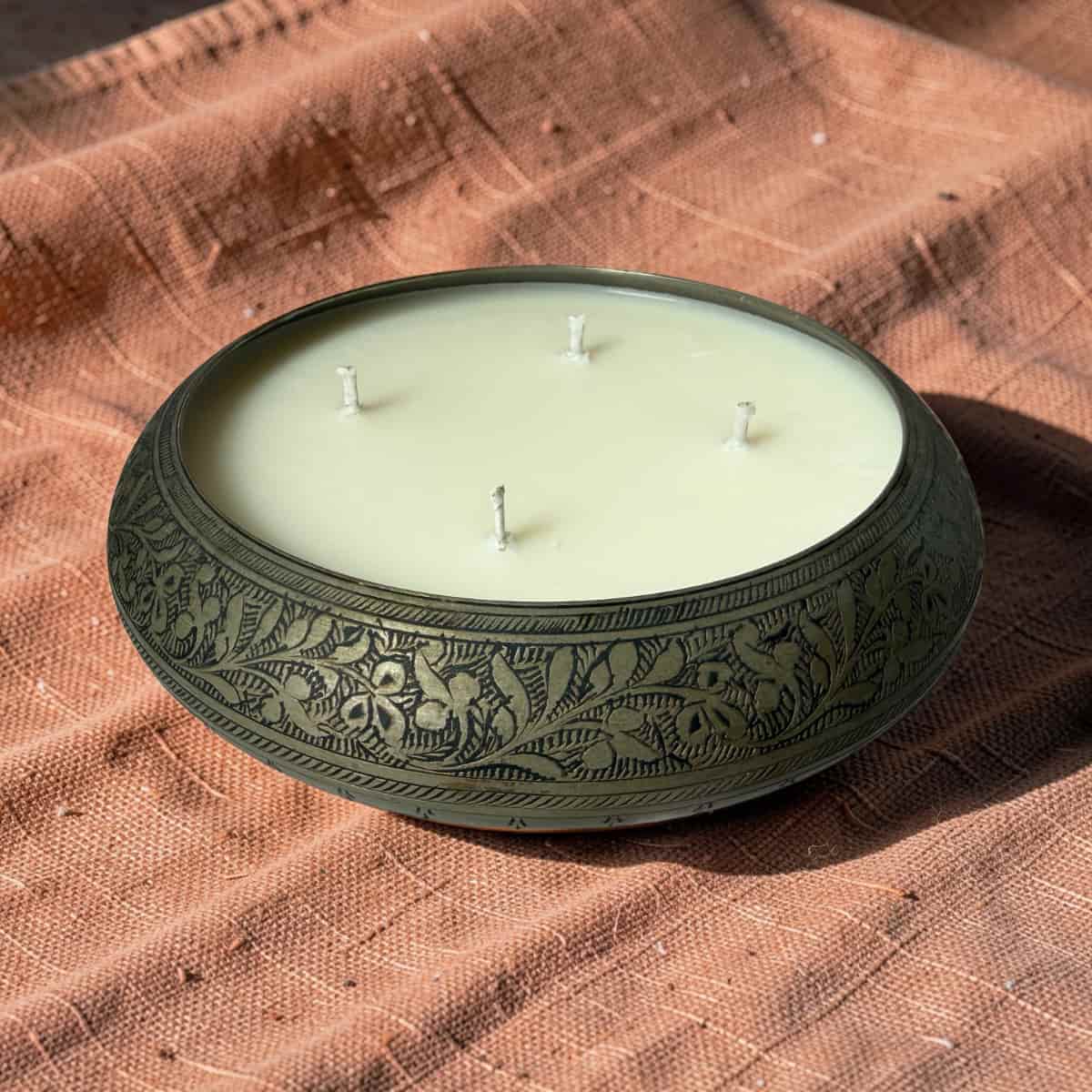 Decorative candle in an embossed metal holder on a brown fabric background