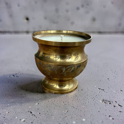 A brass candle holder with an engraved floral pattern, holding a white wax candle, set on a textured gray surface.
