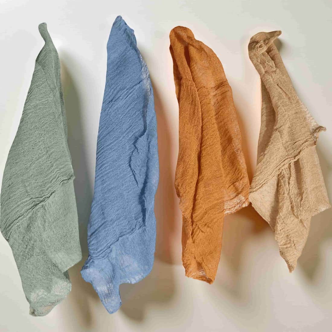 Four textured cloths in green, blue, orange, and beige on a light background