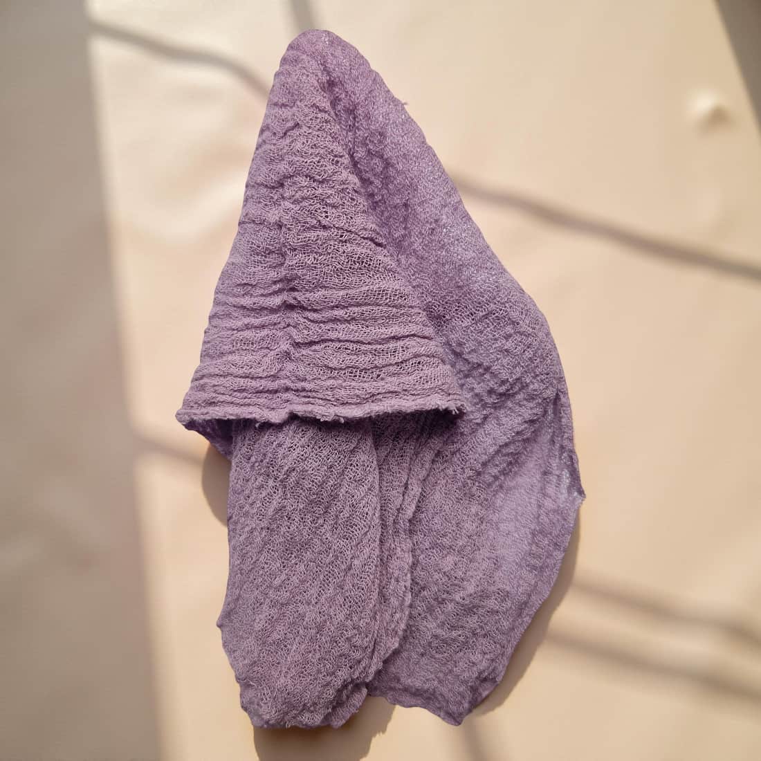 Purple textured towel draped over a beige surface with shadows cast by leaves.
