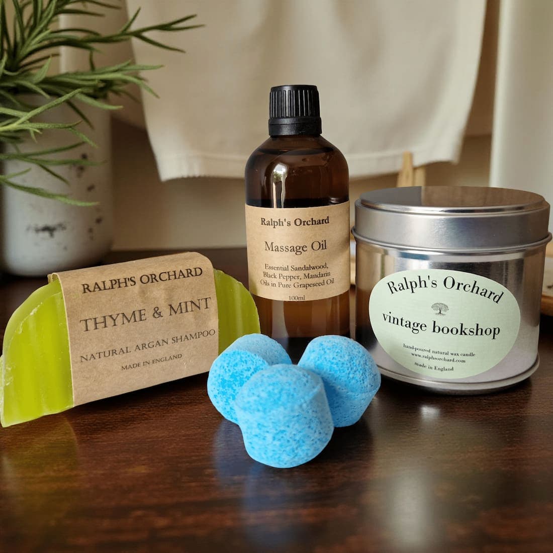 Collection of Ralph's Orchard products including a bottle, candle, soap, and bath bombs on a wooden surface.