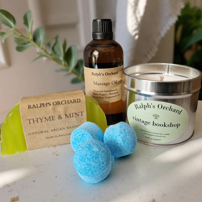 Collection of Ralph's Orchard products including a candle, oil, soap, and bath bombs on a surface.