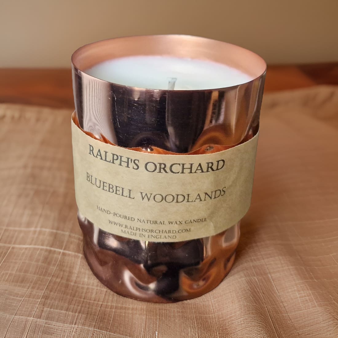Candle in a copper container with a label on a woven surface
