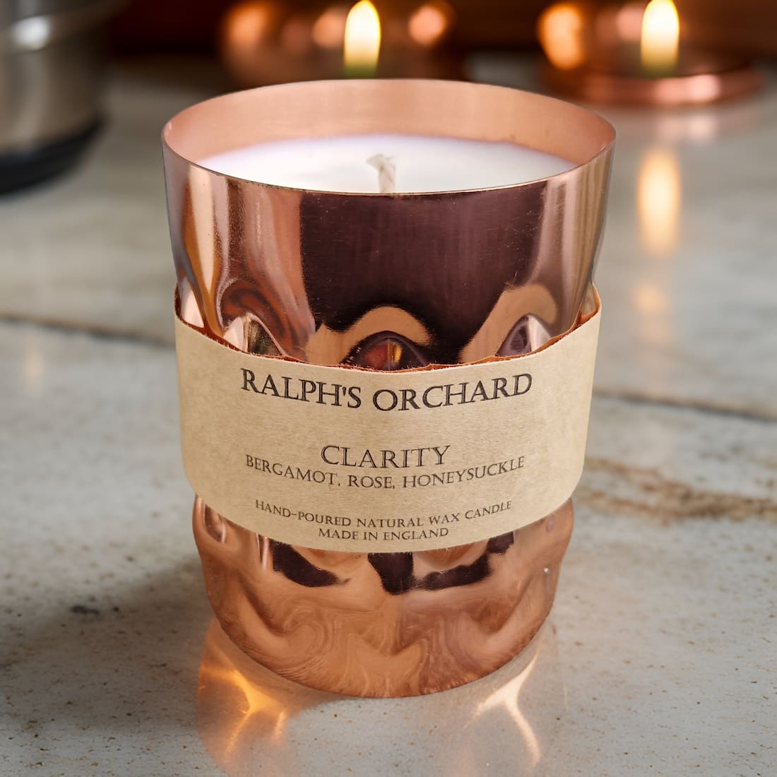 Candle in a copper holder with 'Ralph's Orchard' label on a wooden surface.