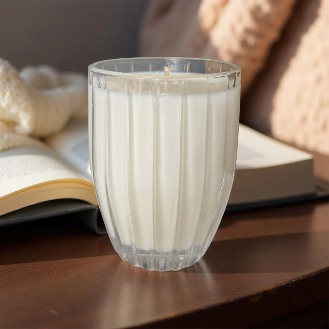 Candle in a glass holder on a wooden surface with an open book and textured fabric in the background