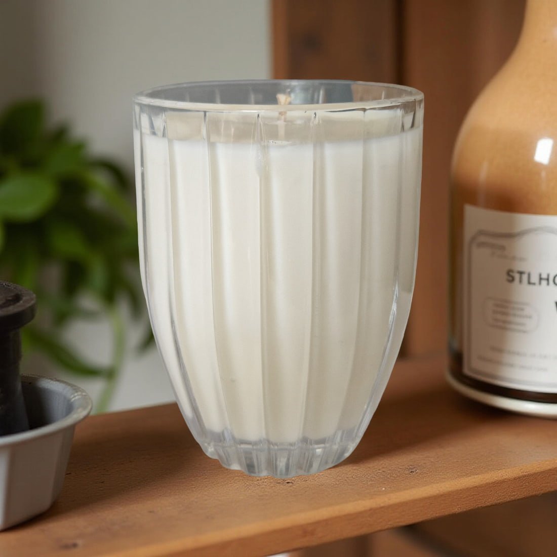 Clear glass vase candle with ribbed design on a wooden shelf with a blurred background