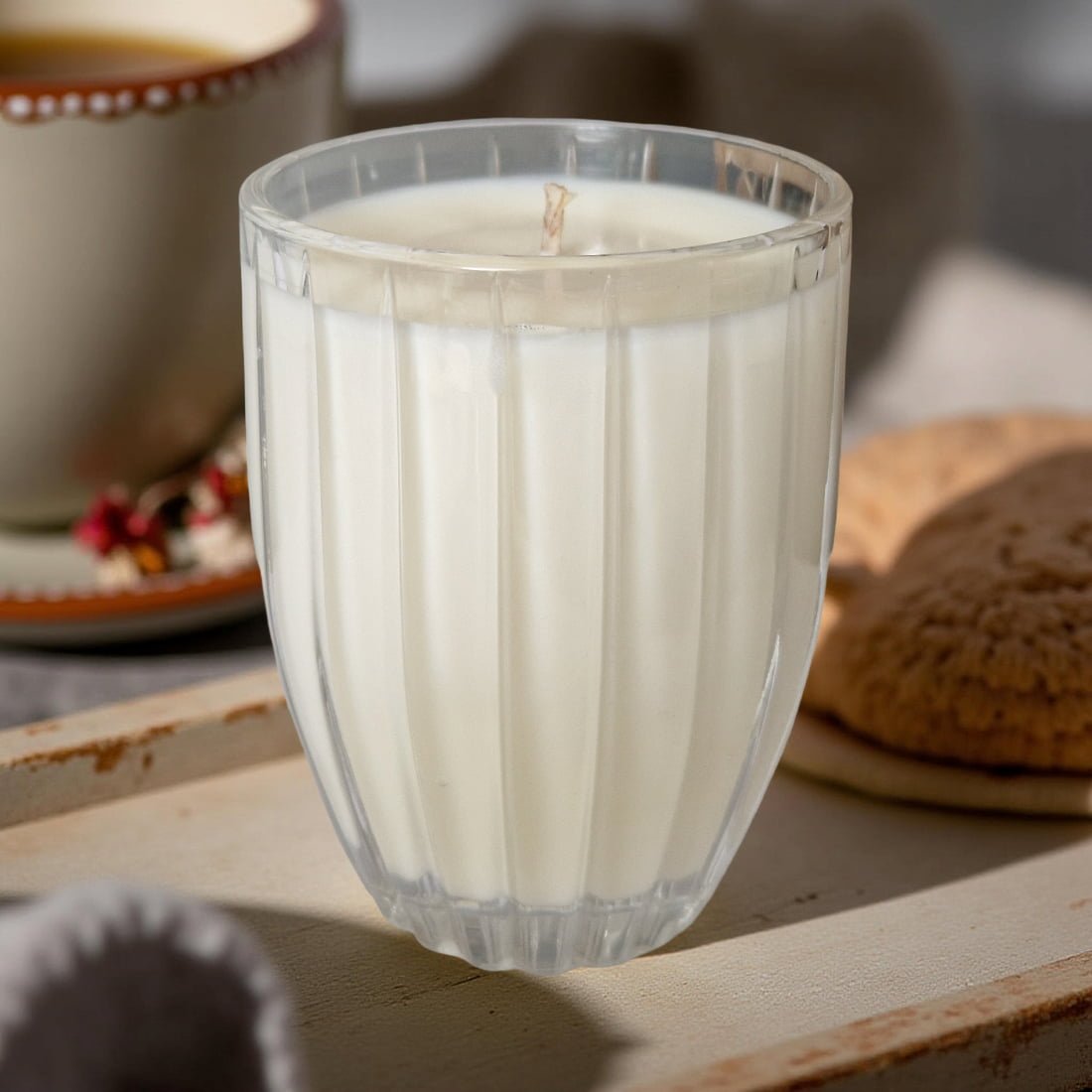 Clear glass candle on a wooden surface with cookies in the background