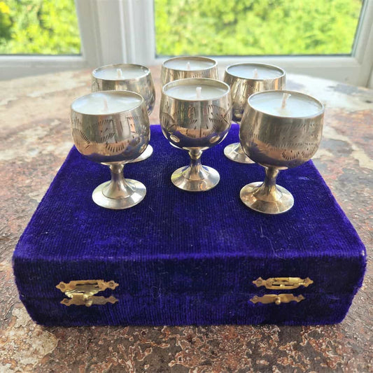 Silver goblet-shaped candles on a purple velvet box with a window in the background