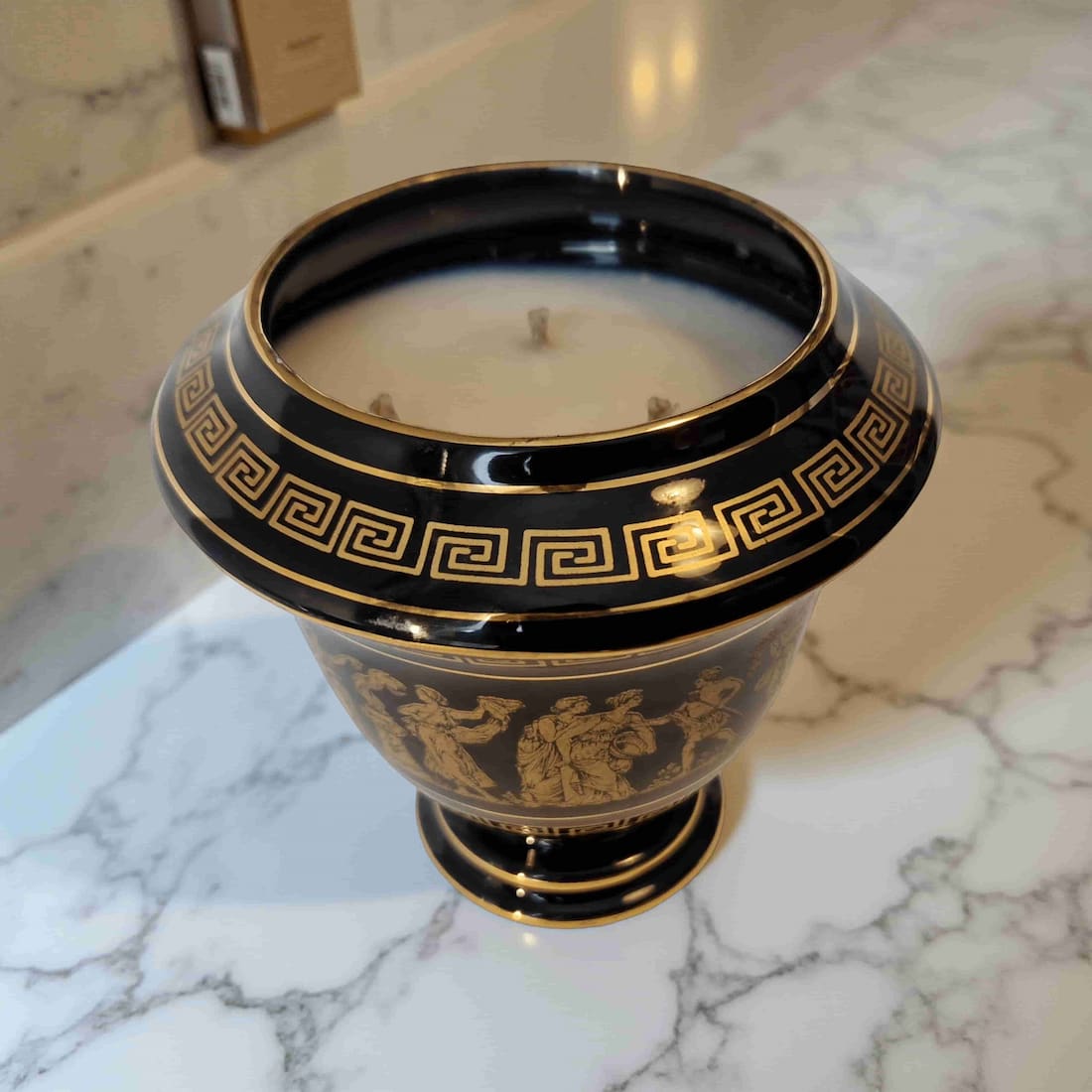 Decorative black and gold candle holder with a candle on a marble surface