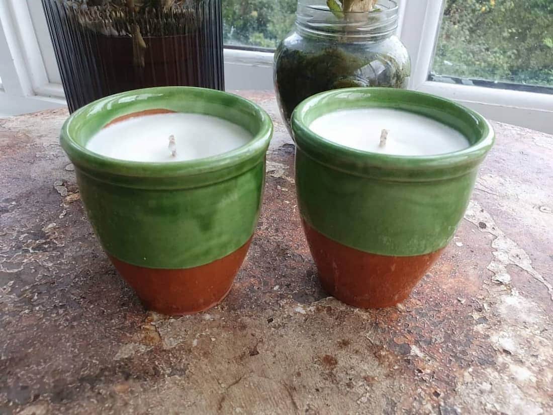 Two green and brown ceramic pots with candles inside on a surface.