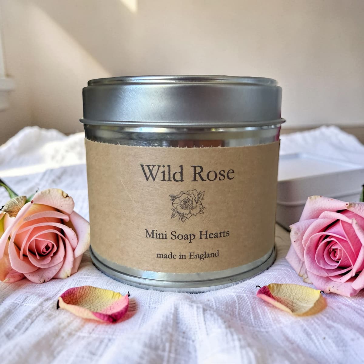 Tin of Wild Rose Mini Soap Hearts with pink roses and rose petals on a white fabric background