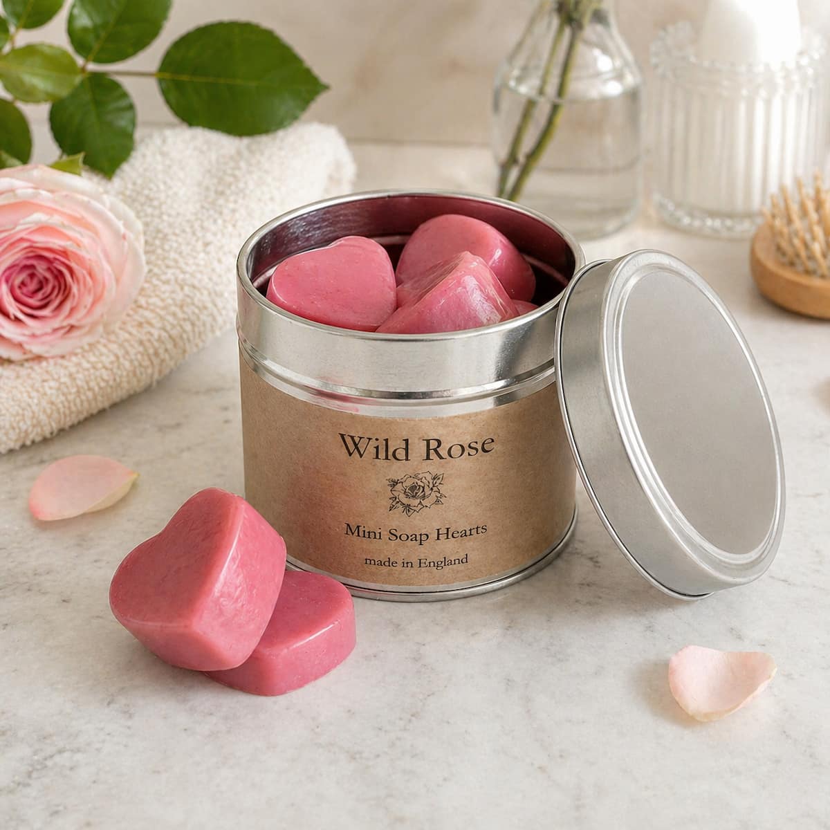 Container of Wild Rose mini soap hearts on a marble surface with a rose and towel in the background.