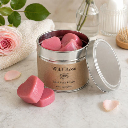Container of Wild Rose mini soap hearts on a marble surface with a rose and towel in the background.