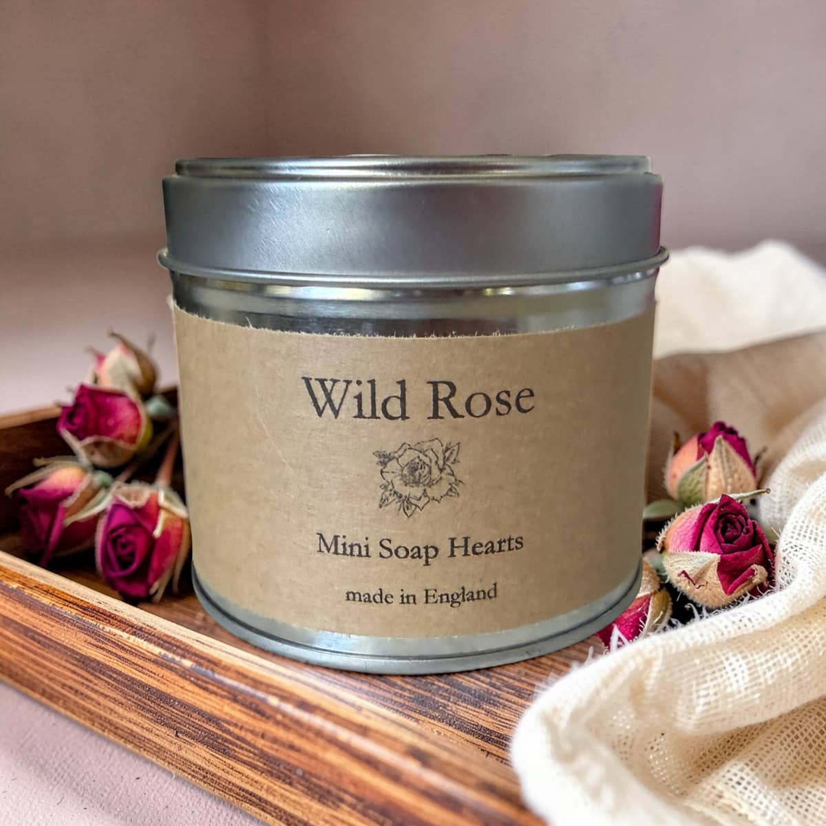 Tin labeled 'Wild Rose Mini Soap Hearts' on a wooden tray with dried roses.