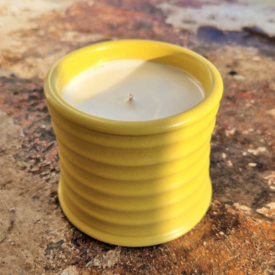 Yellow ceramic container with a candle on a textured surface