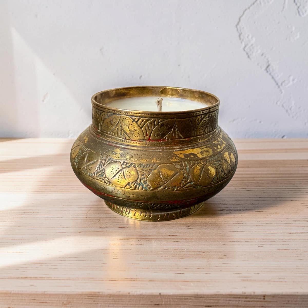 Decorative brass candle holder with a lit candle on a wooden surface.