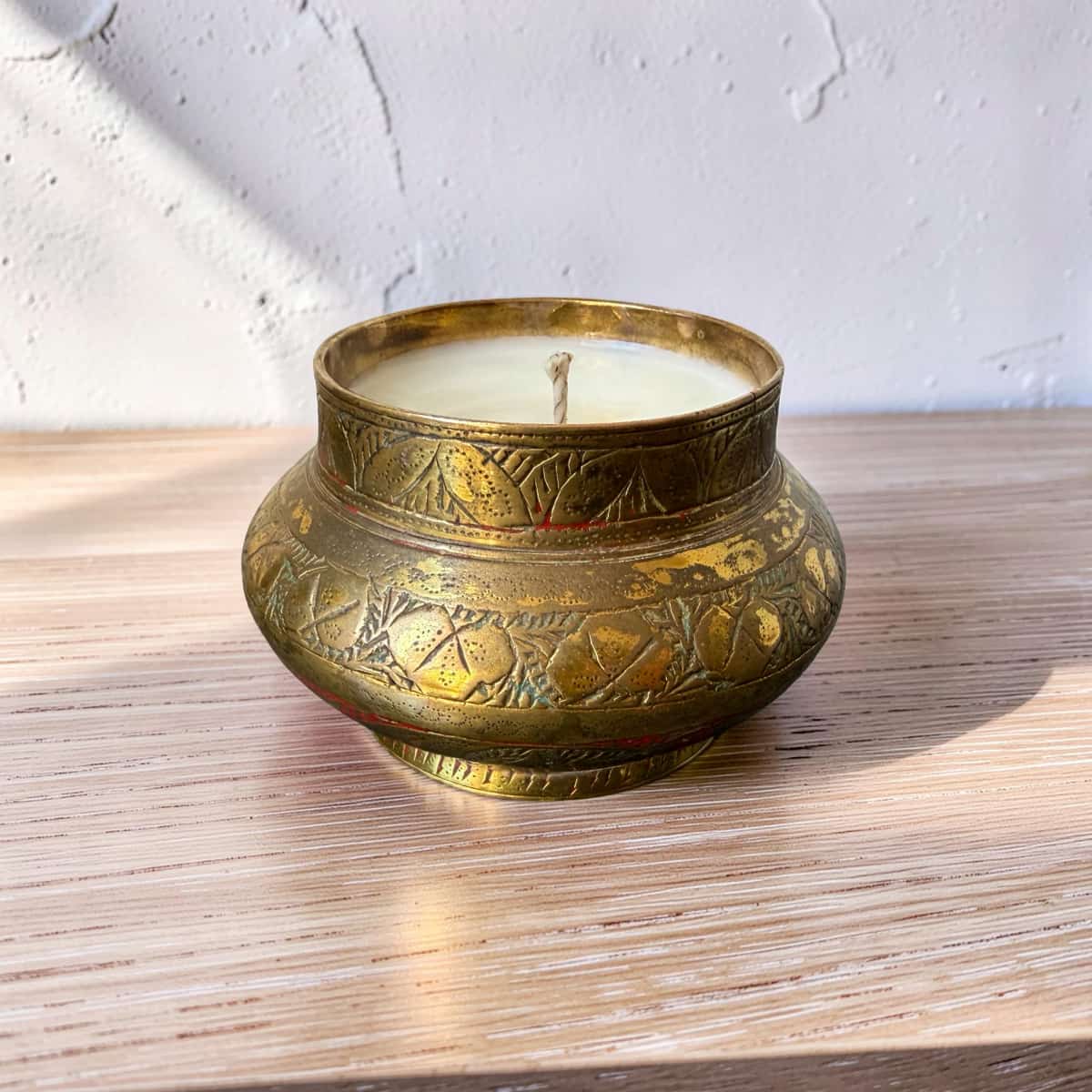 Decorative brass container with a lit candle on a wooden surface
