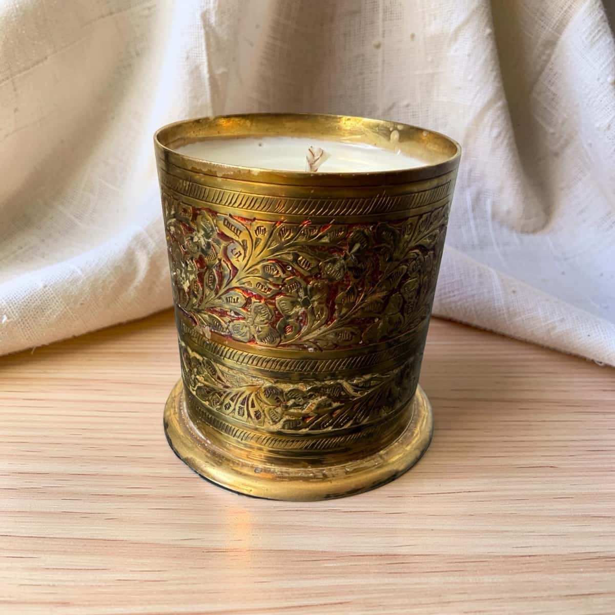 Decorative candle in an ornate brass holder on a wooden surface with a white fabric background