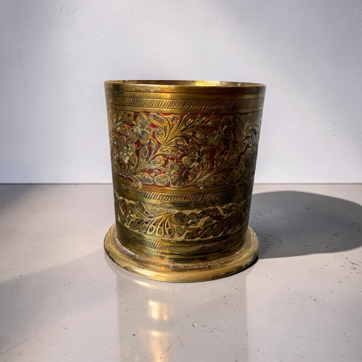Decorative brass cup with intricate patterns on a white surface