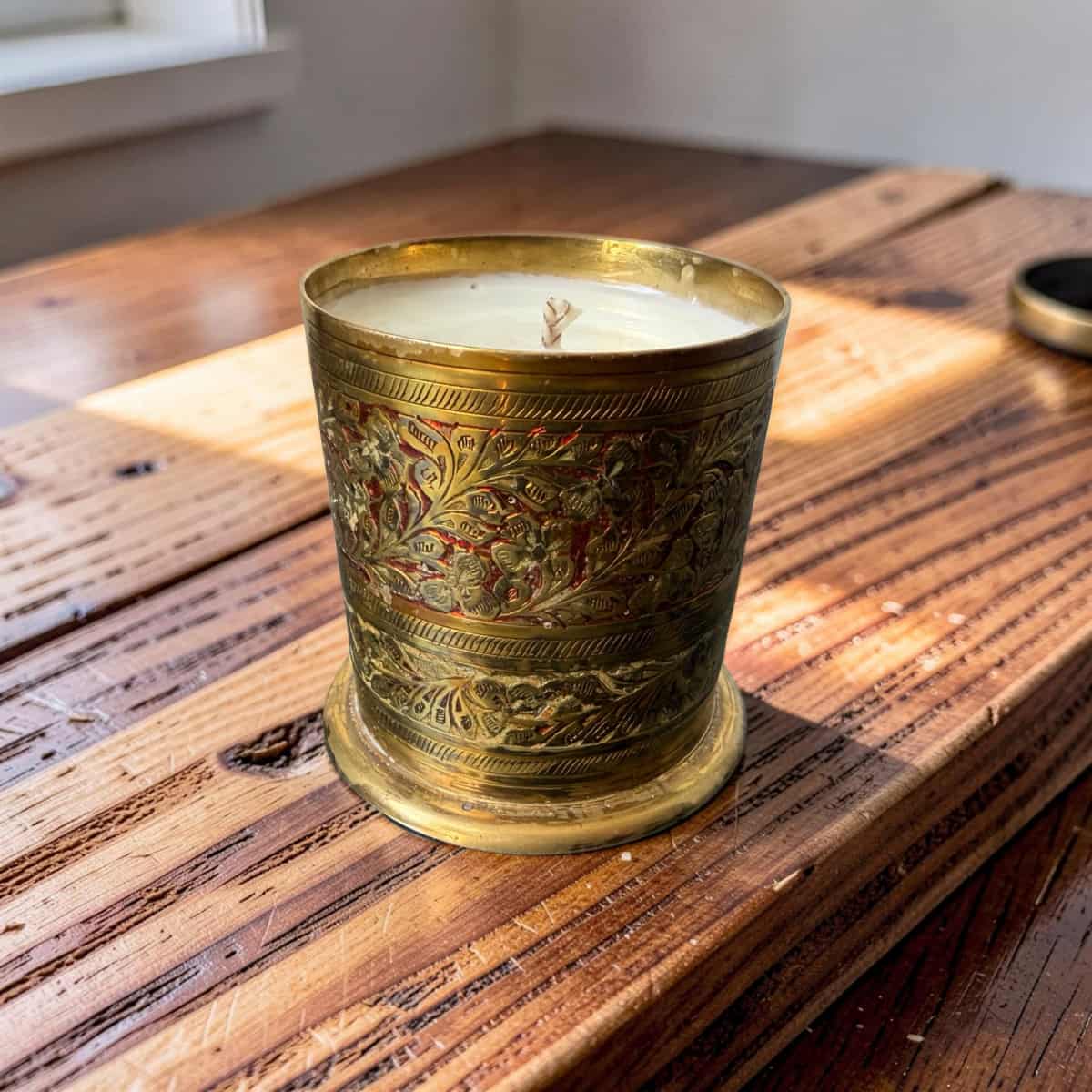 Decorative candle in an ornate brass holder on a wooden surface