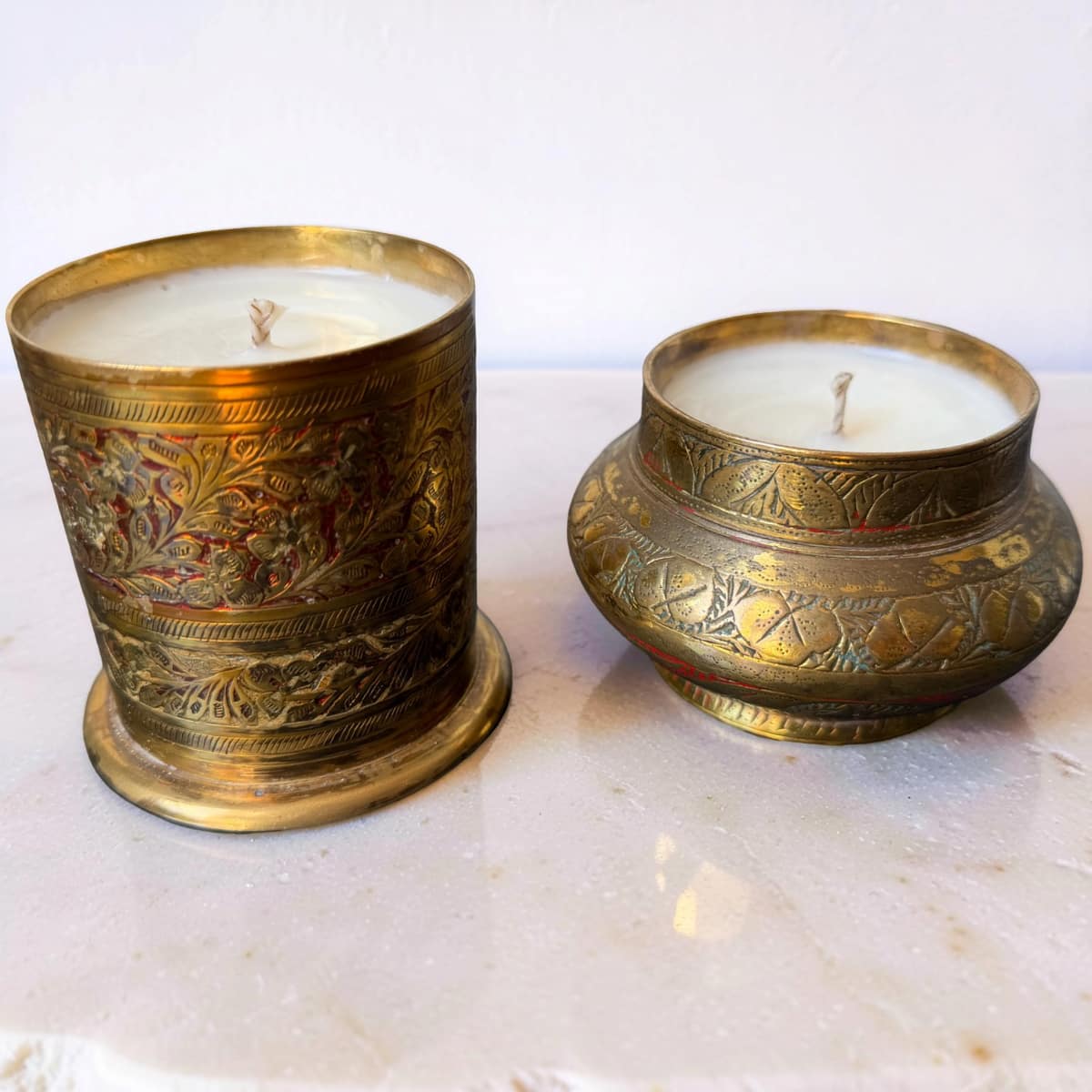 Two ornate brass candle holders with candles on a marble surface.