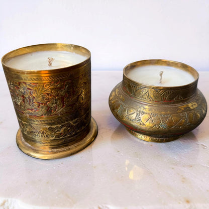 Two ornate brass candle holders with candles on a marble surface.