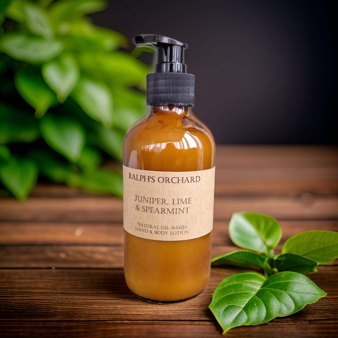 Bottle of Ralph's Orchard Juniper, Lime & Spearmint lotion on a wooden surface with green leaves.