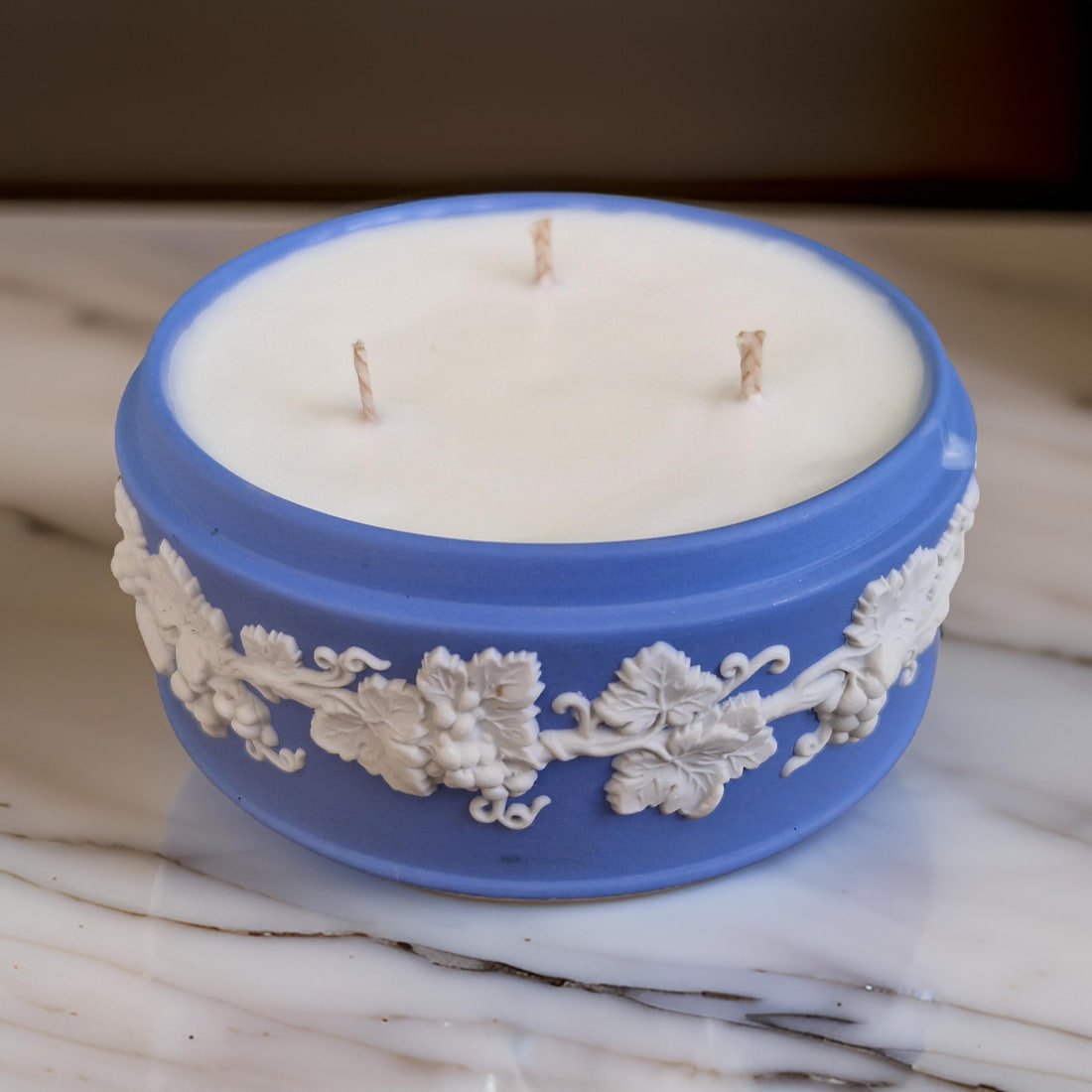 Decorative candle in a blue holder with intricate designs on a marble surface.