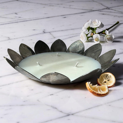 Decorative candle with leaf-like design on a marble surface with flowers and citrus slices.